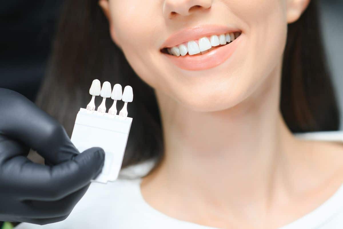 Smiling woman holding dental implant model while wearing black gloves in dental office setting.