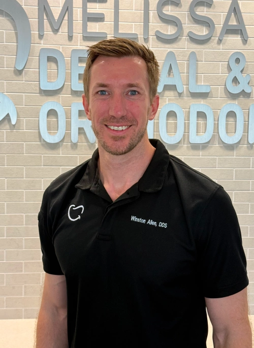 Identical portrait of Dr. Winston Allen wearing a black polo shirt embroidered with "Winston Allen, DDS", standing in front of a light gray brick office wall.